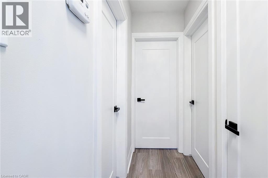 Hallway featuring wood-finish flooring, white paneled doors, and matte black hardware - 103 East 45Th Street, Hamilton, ON - Indoor Photo Showing Other Room