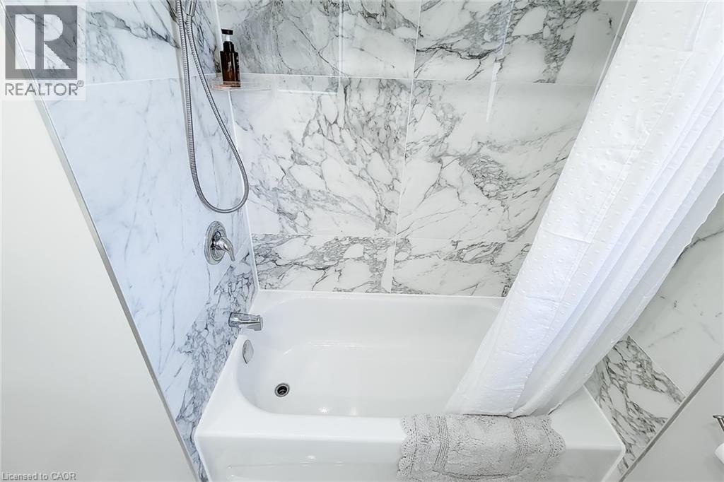 White soaking tub with chrome fixtures, surrounded by large format marble-look tile walls - 103 East 45Th Street, Hamilton, ON - Indoor Photo Showing Bathroom
