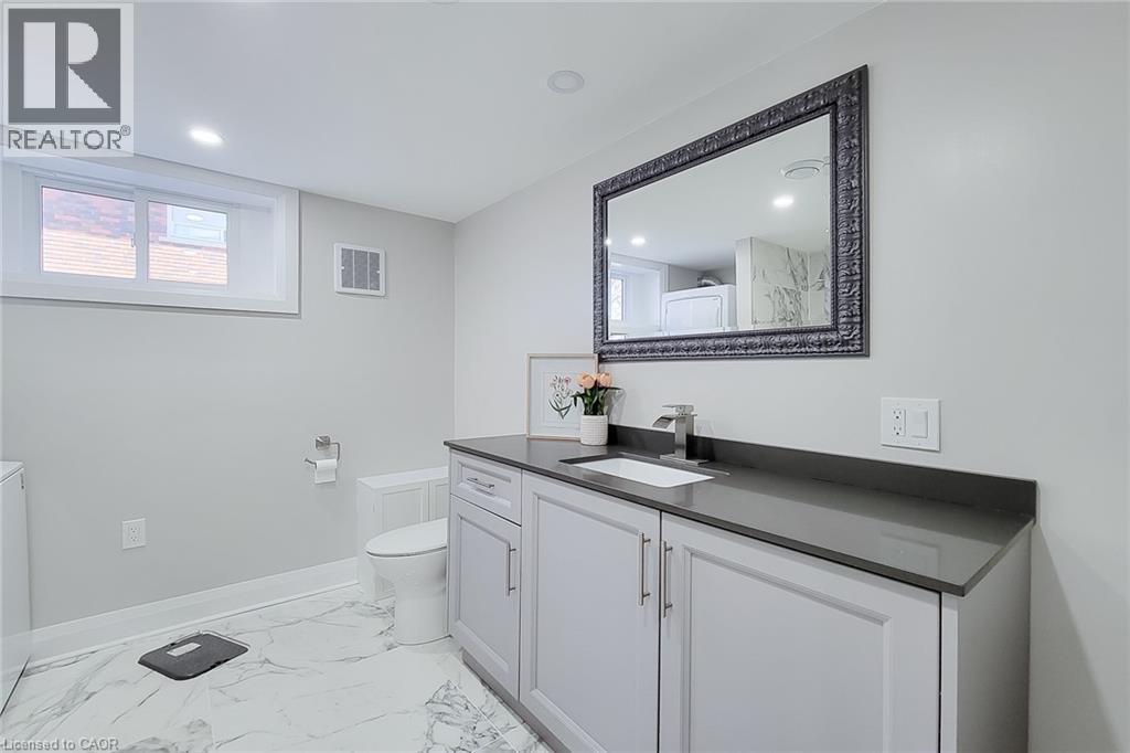 Contemporary bathroom featuring a white vanity with shaker-style cabinetry, a gray solid surface countertop, and a rectangular undermount sink with a chrome faucet - 103 East 45Th Street, Hamilton, ON - Indoor Photo Showing Bathroom