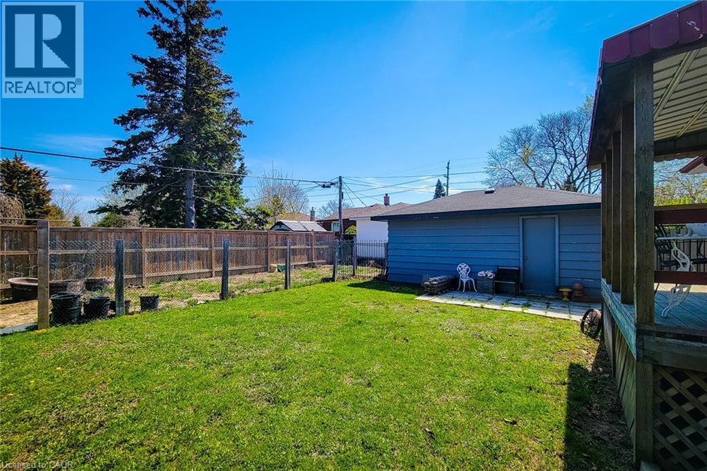 Expansive backyard featuring a lush lawn, privacy fencing, a separate storage structure with a shingled roof, a paved patio area, and a covered wood-decked patio - 103 East 45Th Street, Hamilton, ON - Outdoor