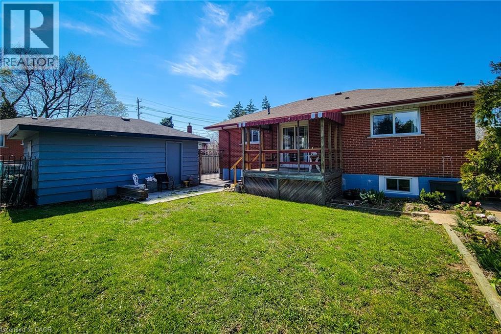 Spacious backyard featuring a detached garage with siding, a brick exterior home, a wooden deck with a red awning, and a grass lawn - 103 East 45Th Street, Hamilton, ON - Outdoor