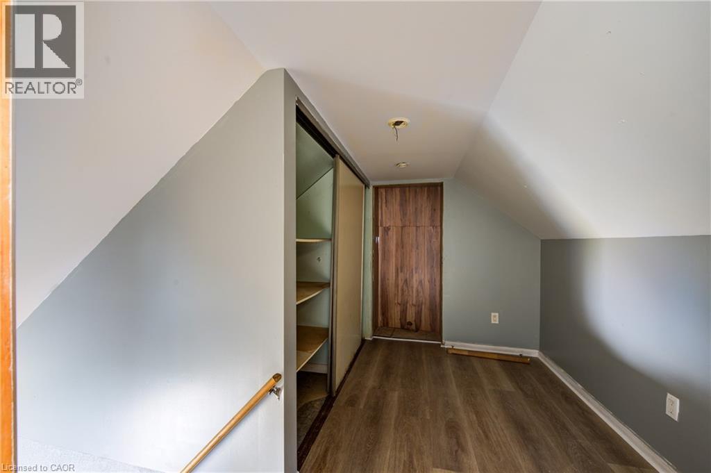 Loft space featuring wood-finish flooring, built-in shelving with sliding doors, a natural wood door, and sloped ceilings - 1 Rathgar Street, London, ON - Indoor Photo Showing Other Room