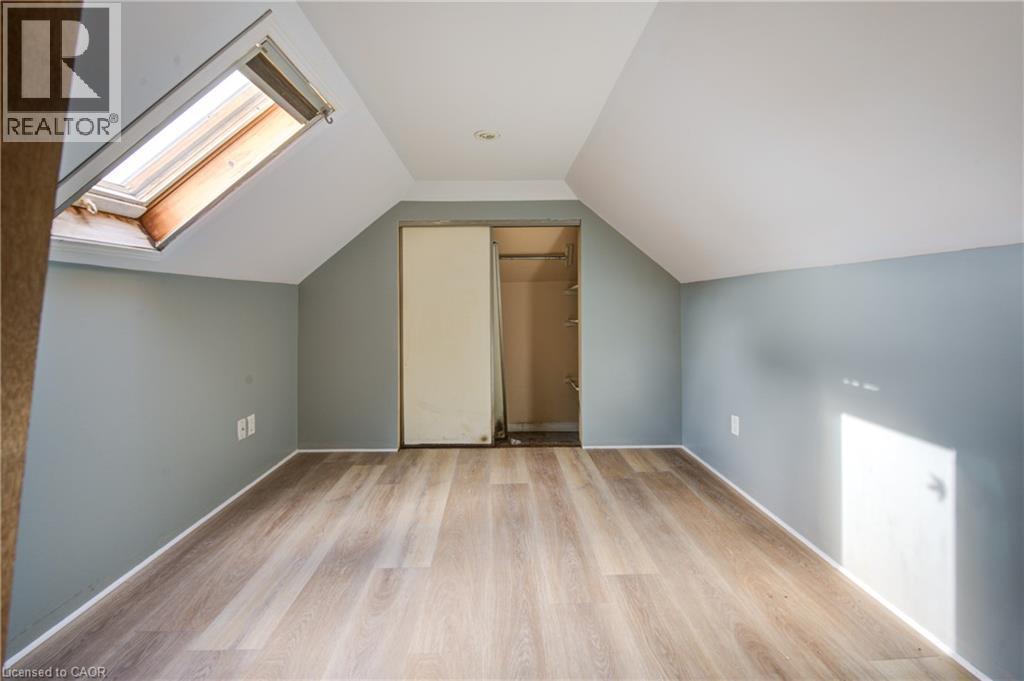 Bedroom 2 featuring a skylight with a retractable shade, wood-finish flooring, light grey painted walls, sloped white ceilings, and a built-in closet with sliding doors - 1 Rathgar Street, London, ON - Indoor Photo Showing Other Room