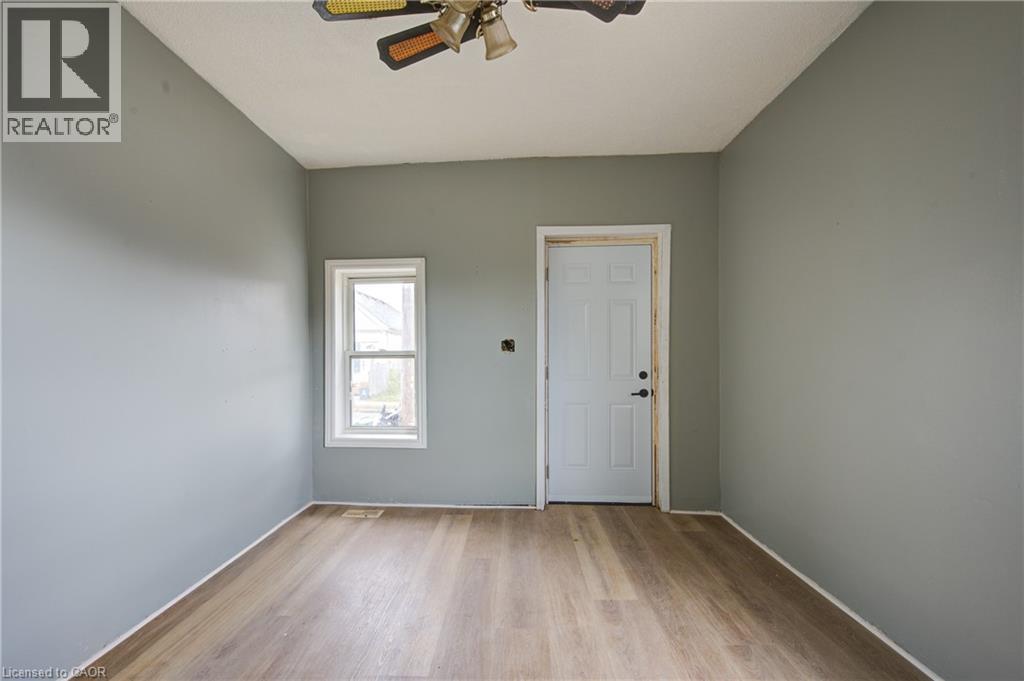 Unit 1A Living Room; Light gray walls complement the wood-finish flooring in this room featuring a white paneled door, a single window with white trim, and an overhead ceiling fan - 1 Rathgar Street, London, ON - Indoor Photo Showing Other Room