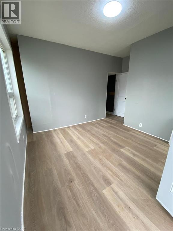 Unit 1A Living Room; Spacious room featuring light wood-finish flooring, neutral gray wall tones, white trim, and a ceiling-mounted light fixture - 1 Rathgar Street, London, ON - Indoor Photo Showing Other Room