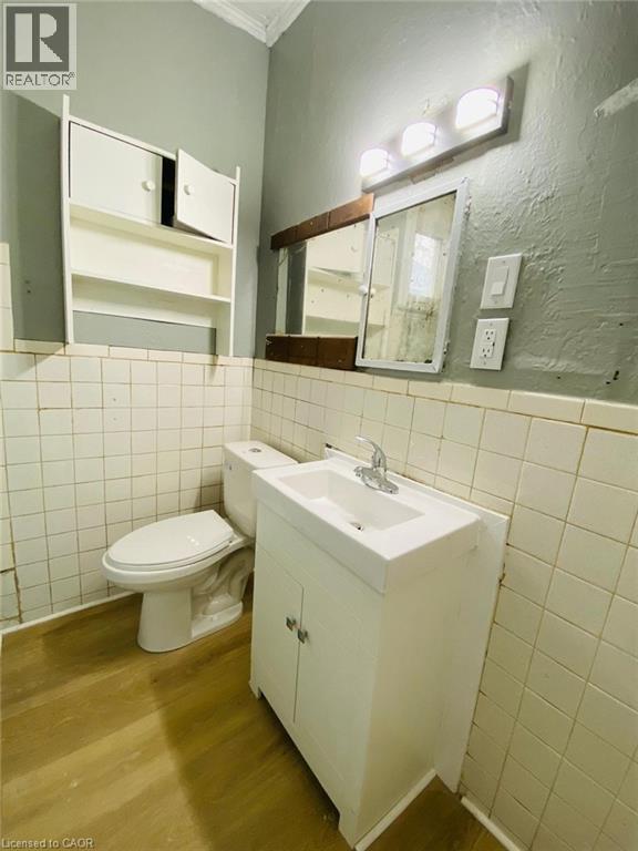 Unit 1A - 4 Pc Bathroom featuring wood-finish flooring, white square wall tile, and a white vanity with integrated sink - 1 Rathgar Street, London, ON - Indoor Photo Showing Bathroom