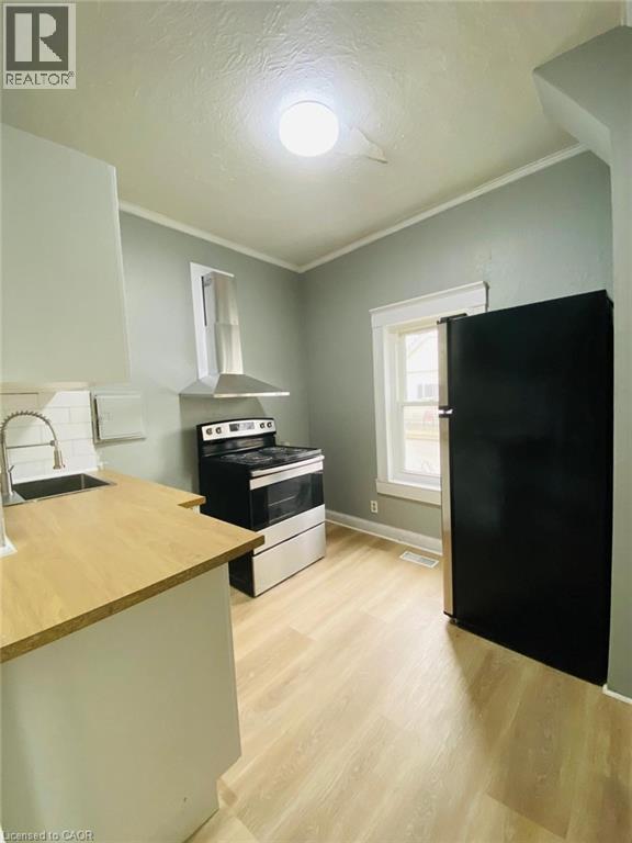 Unit 1A Kitchen featuring wood-finish flooring, light-toned cabinetry, stainless steel range with overhead ventilation, and a black refrigerator - 1 Rathgar Street, London, ON - Indoor Photo Showing Other Room