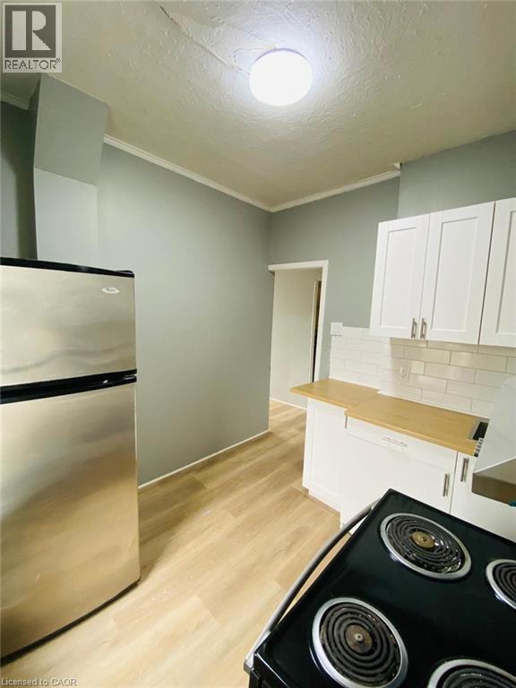 Unit 1A Kitchen featuring light wood-finish flooring, white cabinetry, a subway tile backsplash, and a stainless steel refrigerator - 1 Rathgar Street, London, ON - Indoor Photo Showing Kitchen