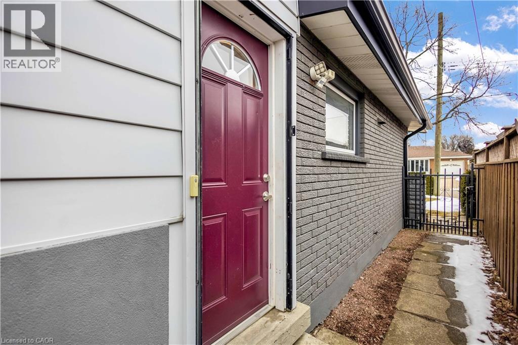 Exterior entry featuring a red paneled door with an arched transom window, white horizontal siding, and a contrasting gray brick facade - 85 Ranchdale Drive, Hamilton, ON - Outdoor With Exterior