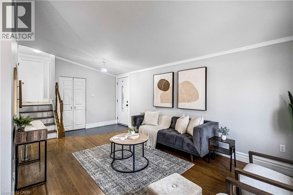 Living area featuring wood-finish flooring, light gray wall tones, white trim, and a white front entry door with decorative glass - 85 Ranchdale Drive, Hamilton, ON