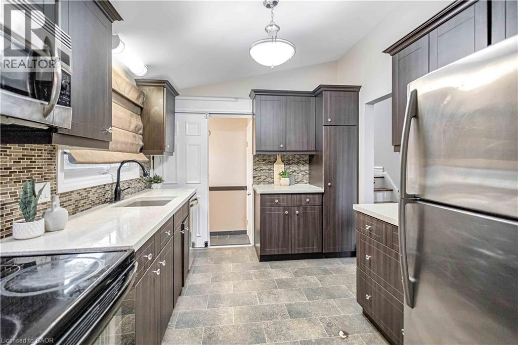 Contemporary kitchen featuring wood-finish cabinetry, light-toned countertops, and a mosaic tile backsplash - 85 Ranchdale Drive, Hamilton, ON
