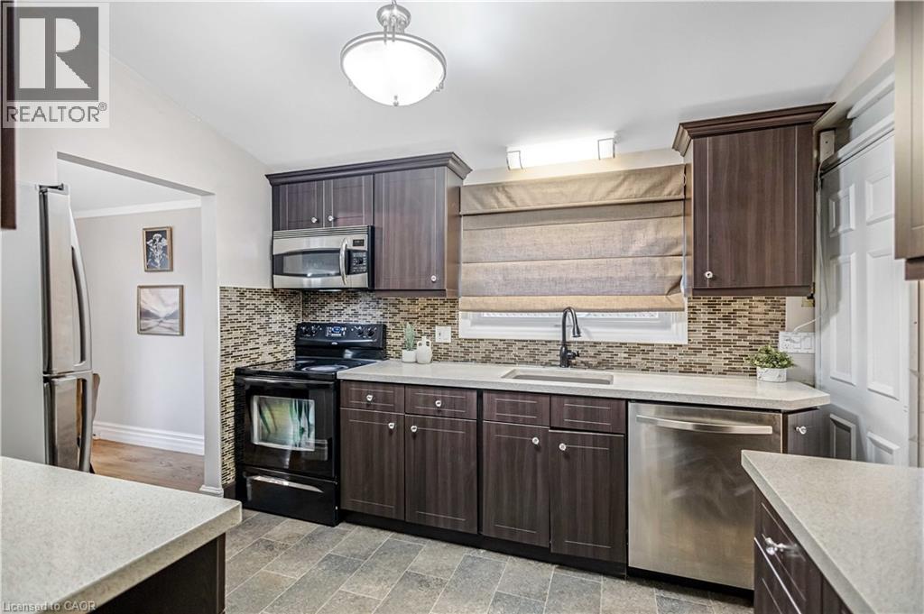 Contemporary kitchen featuring dark wood-finish cabinetry, light-toned countertops, a mosaic tile backsplash, stainless steel appliances, and diagonal tile flooring - 85 Ranchdale Drive, Hamilton, ON