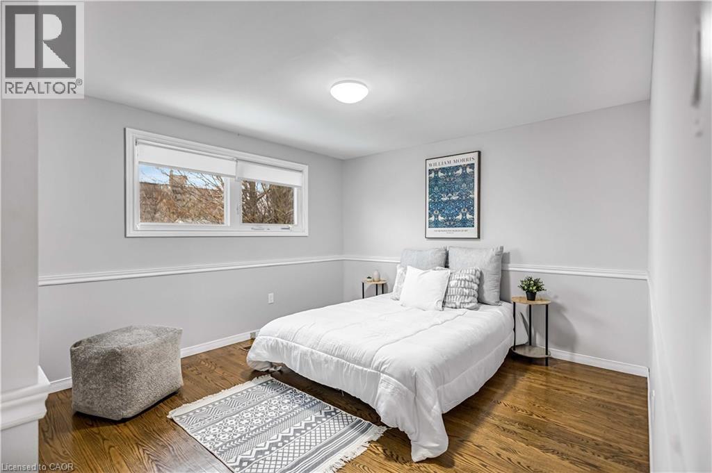 Bedroom featuring wood-finish flooring, two large windows, a white ceiling light fixture, and two-tone wall paint with chair rail trim - 85 Ranchdale Drive, Hamilton, ON