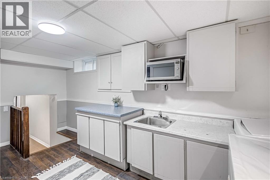 Compact kitchen area featuring white cabinetry, a built-in microwave, a stainless steel sink, and light-toned countertops - 85 Ranchdale Drive, Hamilton, ON