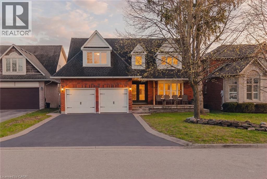 Brick and siding exterior featuring a double-car garage with white doors, a paved driveway, and a covered front porch - 79 Holbrook Crescent, Cambridge, ON - Outdoor With Facade
