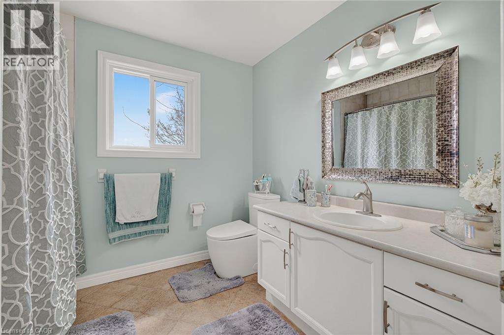 Bathroom featuring a single vanity with white cabinetry and a light-toned countertop, a rectangular mirror with a decorative frame, and a four-light fixture - 79 Holbrook Crescent, Cambridge, ON - Indoor Photo Showing Bathroom