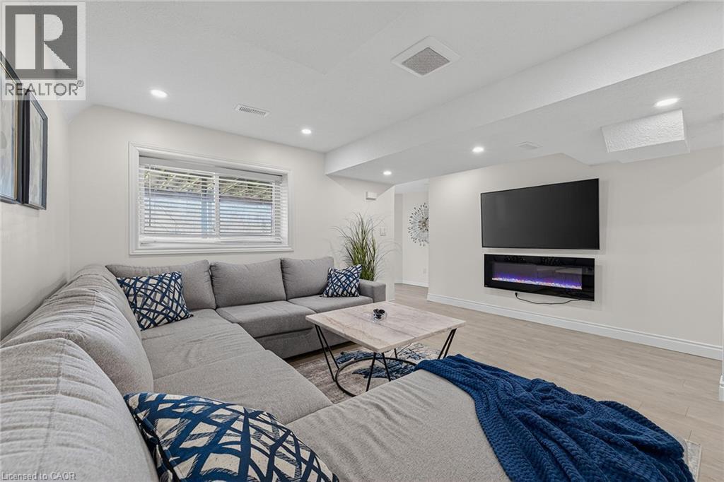 Bright living space featuring recessed lighting, a modern wall-mounted electric fireplace, wood-finish flooring, and a large window with blinds - 79 Holbrook Crescent, Cambridge, ON - Indoor Photo Showing Living Room