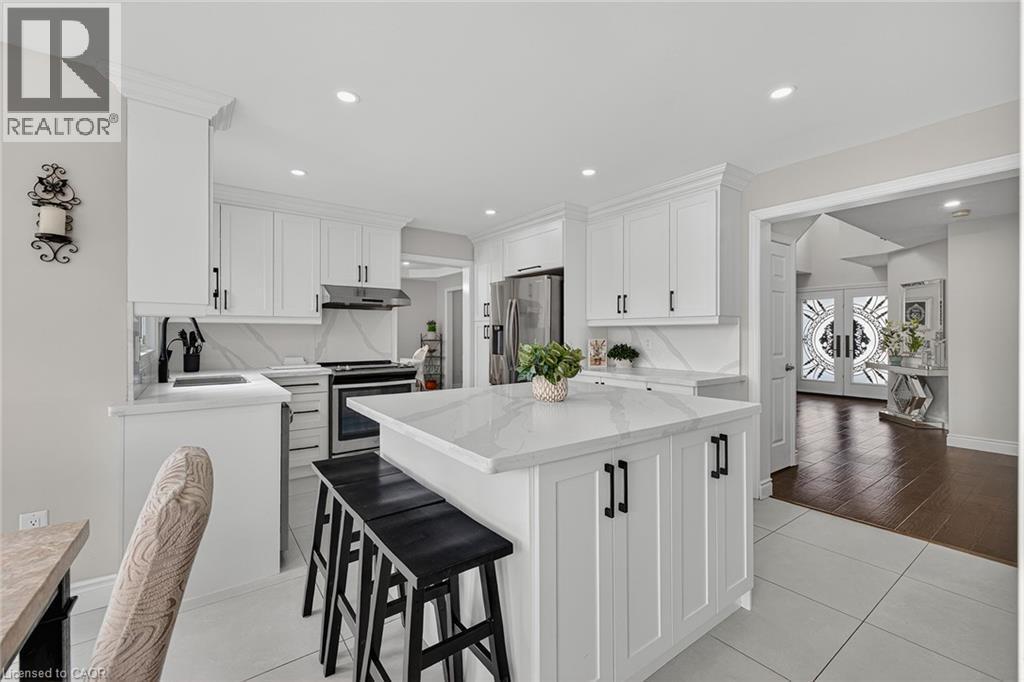 Bright kitchen featuring a central island with countertop seating, white shaker cabinetry, stainless steel appliances, and a matching stone backsplash - 79 Holbrook Crescent, Cambridge, ON - Indoor