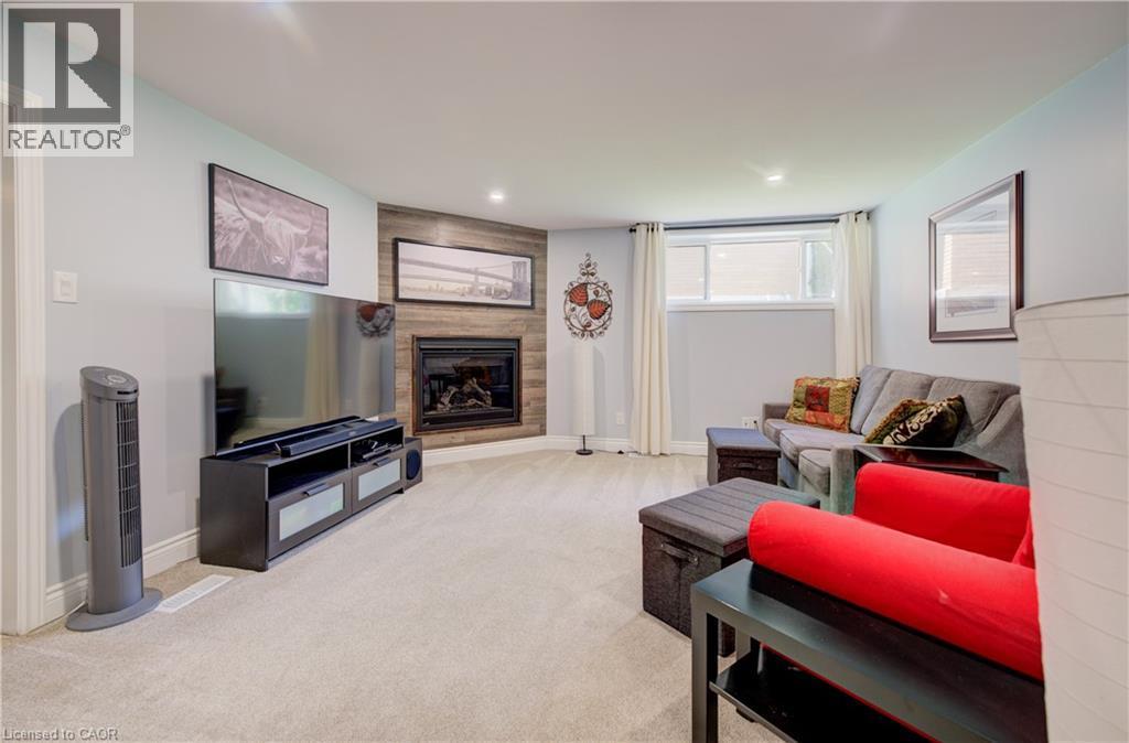 Carpeted living space featuring a corner fireplace with wood-finish paneling, recessed lighting, and a large egress window - 172 Rennie Drive, Kitchener, ON - Indoor Photo Showing Living Room With Fireplace
