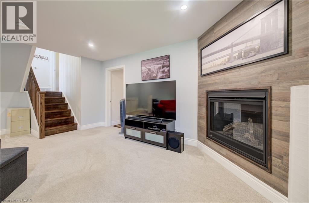 Carpeted recreation area featuring a wood-finish accent wall with an inset fireplace, recessed lighting, and a stained wood staircase with railing - 172 Rennie Drive, Kitchener, ON - Indoor With Fireplace