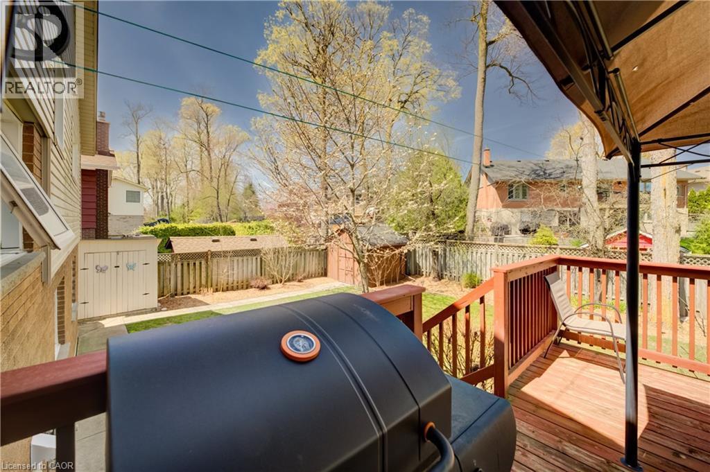 Wood-decked outdoor space featuring a covered section, wood railing, and direct access to a fenced backyard with mature trees - 172 Rennie Drive, Kitchener, ON - Outdoor