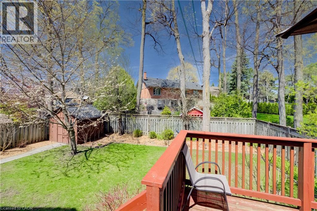 Expansive rear yard featuring a wood-finish deck, a manicured lawn, perimeter fencing, and a detached storage shed - 172 Rennie Drive, Kitchener, ON - Outdoor