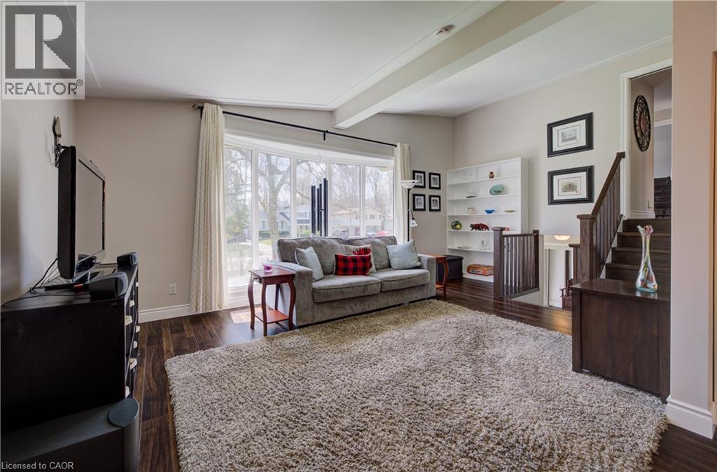 Living area featuring expansive bay windows, rich wood-finish flooring, a built-in white shelving unit, and a prominent staircase with wood railings - 172 Rennie Drive, Kitchener, ON - Indoor Photo Showing Living Room