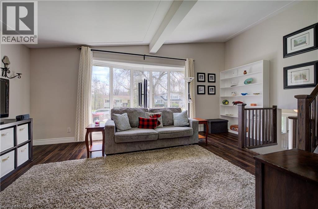 Living area featuring wood-finish flooring, a large bay window, a built-in white shelving unit, and dark wood stair railings - 172 Rennie Drive, Kitchener, ON - Indoor Photo Showing Living Room