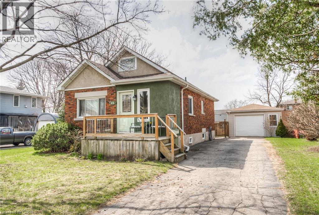 Brick and stucco exterior featuring a front deck with wood railing, a paved driveway, and a detached garage with an overhead door - 46 2 Avenue, Kitchener, ON - Outdoor With Deck Patio Veranda