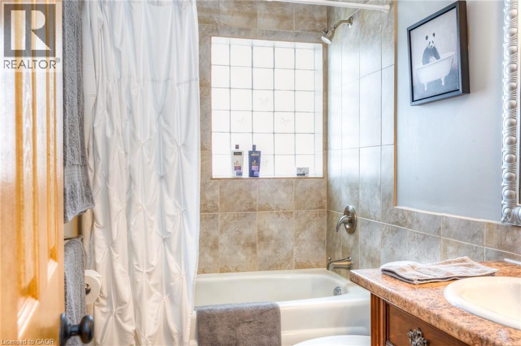 Full bathroom featuring a tub/shower combination with tile surround, a glass block window, and a vanity with an integrated sink and wood-finish cabinetry - 46 2 Avenue, Kitchener, ON - Indoor Photo Showing Bathroom