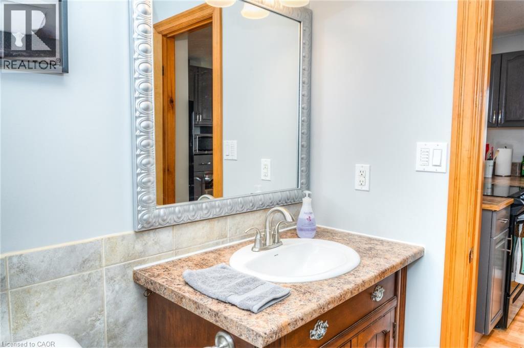 Powder room featuring a decorative framed mirror, single vanity with an integrated sink, and a tiled backsplash - 46 2 Avenue, Kitchener, ON - Indoor Photo Showing Bathroom