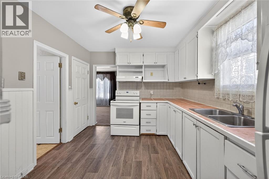 Kitchen featuring white cabinetry, wood-finish flooring, a double basin stainless steel sink, and a white electric range - 192 Ivon Avenue, Hamilton, ON - Indoor Photo Showing Kitchen With Double Sink