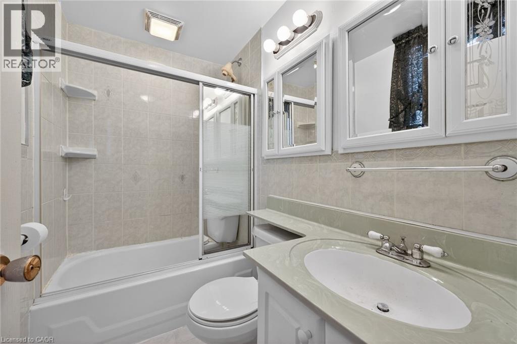 Bathroom featuring a white bathtub with sliding glass doors, light-toned tiled shower surround, a vanity with an integrated sink, and white framed medicine cabinets - 192 Ivon Avenue, Hamilton, ON - Indoor Photo Showing Bathroom