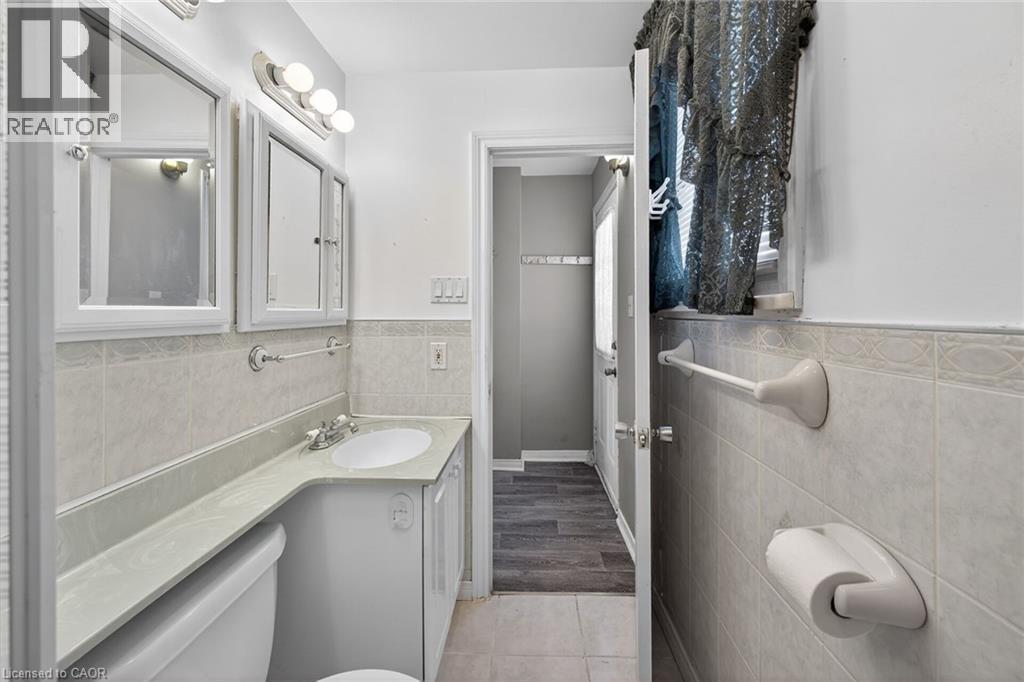 Bathroom featuring a vanity with an integrated sink, dual wall-mounted medicine cabinets, a three-light fixture, and light-toned wall tile - 192 Ivon Avenue, Hamilton, ON - Indoor Photo Showing Bathroom