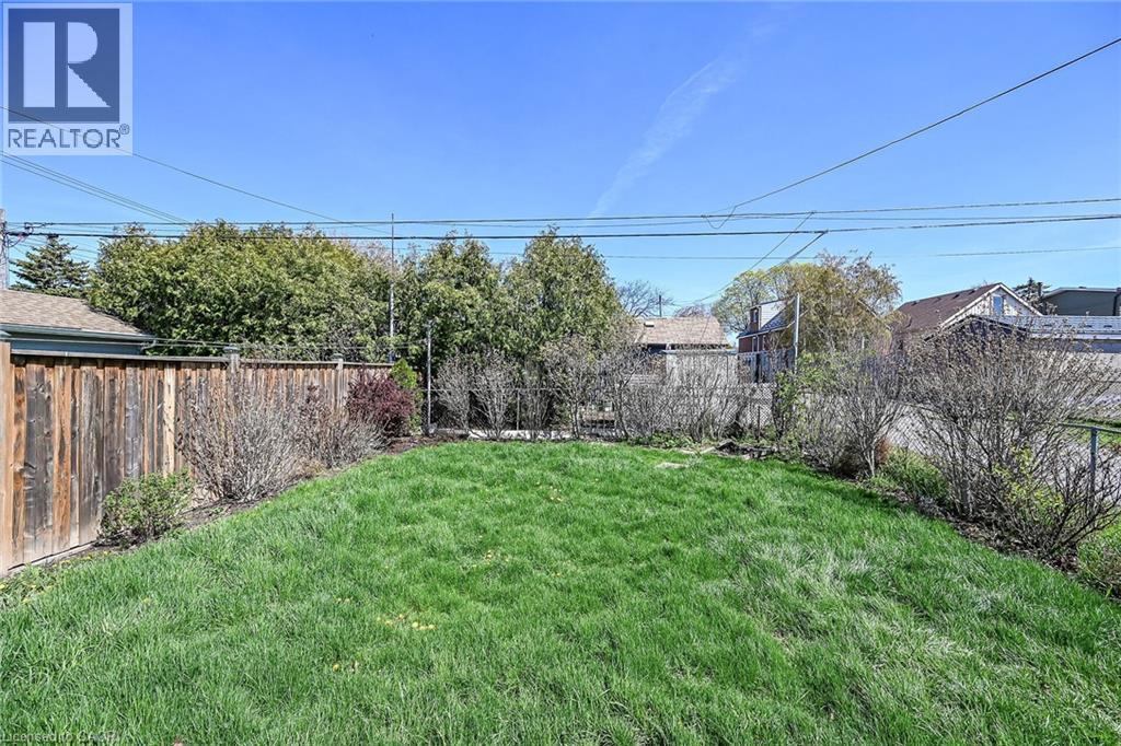 Expansive lawn area featuring a wooden privacy fence, mature trees, and established shrubbery along the perimeter - 192 Ivon Avenue, Hamilton, ON - Outdoor