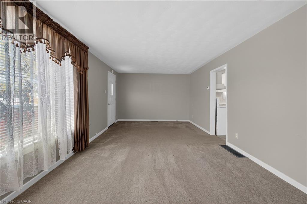 Spacious room featuring neutral paint, carpeted flooring, a large window, and an entry door - 192 Ivon Avenue, Hamilton, ON - Indoor Photo Showing Other Room