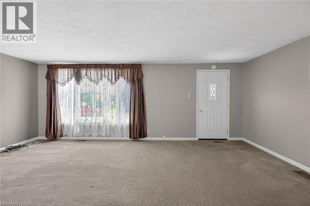 Spacious room featuring carpeting, light gray wall paint, and a large front window with a decorative valance - 192 Ivon Avenue, Hamilton, ON - Indoor Photo Showing Other Room