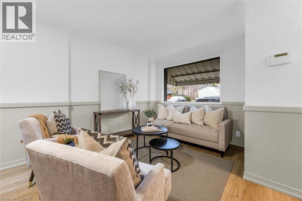 Living area featuring light wood-finish flooring, two-tone wall treatment with wainscoting, and a large window providing natural light - 11 Ford Street, Hamilton, ON - Indoor Photo Showing Living Room