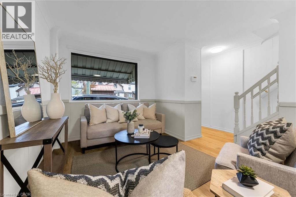 Living area featuring wood-finish flooring, a large window, a chair rail, and a visible staircase with painted handrail and balusters - 11 Ford Street, Hamilton, ON - Indoor Photo Showing Living Room