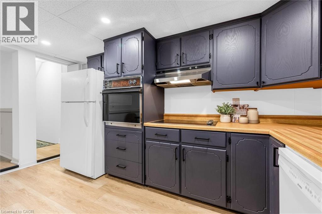 Kitchen featuring dark-toned cabinetry with decorative trim, wood-finish countertops, built-in wall oven, stainless steel range hood, and light wood-finish flooring - 11 Ford Street, Hamilton, ON - Indoor Photo Showing Kitchen
