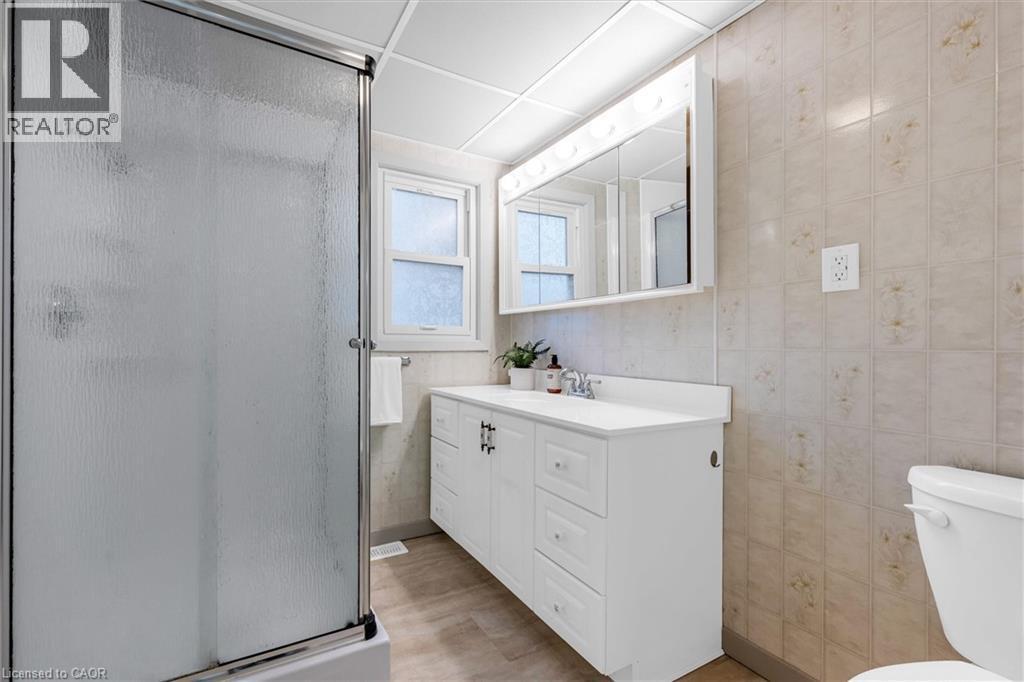 Bathroom featuring a textured glass shower enclosure with chrome framing, a white vanity with integrated sink, a mirrored medicine cabinet with integrated lighting, a window with frosted glass, and ne - 11 Ford Street, Hamilton, ON - Indoor Photo Showing Bathroom