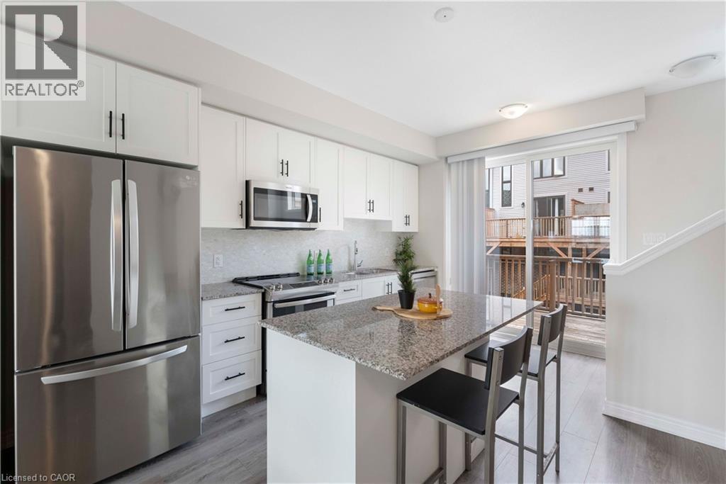 Modern kitchen featuring white shaker cabinetry, stainless steel appliances, a stone countertop island with seating, a mosaic tile backsplash, and wood-finish flooring - 50 Hollywood Court, Cambridge, ON - Indoor Photo Showing Kitchen With Stainless Steel Kitchen