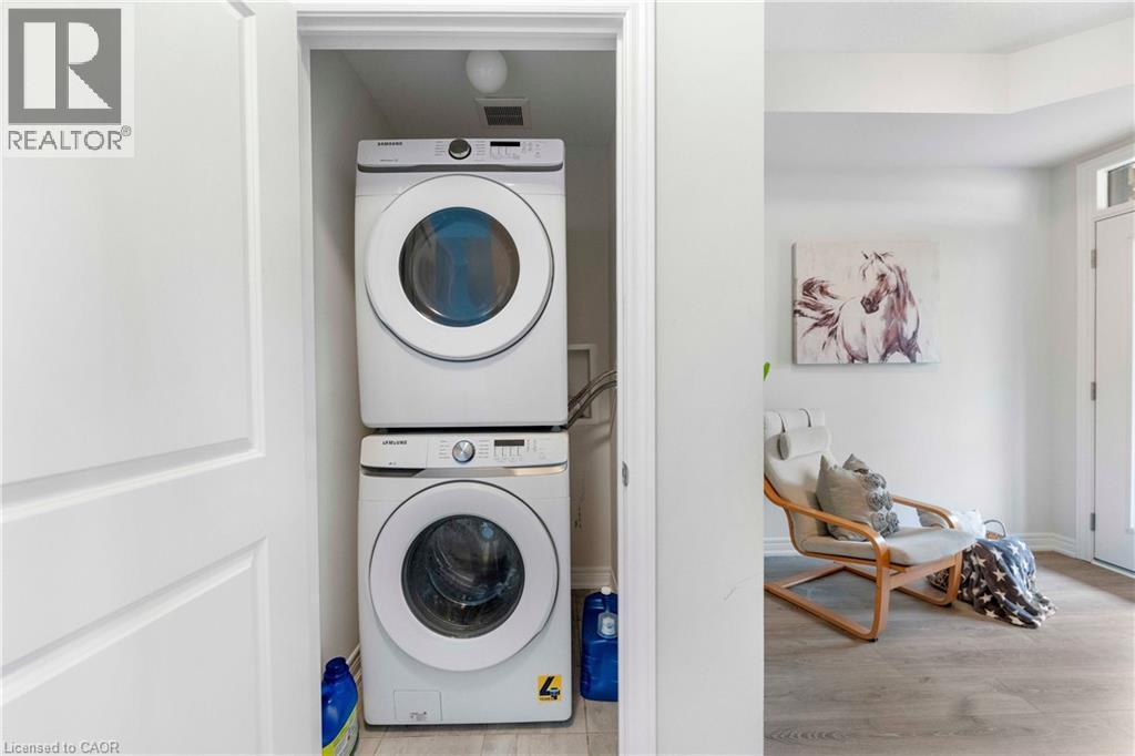 Dedicated laundry closet featuring a stacked white washer and dryer unit, overhead lighting, and light wood-finish flooring - 50 Hollywood Court, Cambridge, ON - Indoor Photo Showing Laundry Room