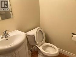 Bathroom featuring a white toilet, coordinating vanity with integrated sink, chrome faucet, and wood-finish flooring -