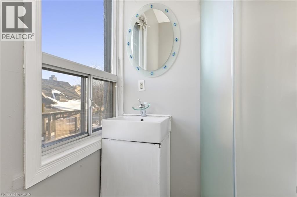 White vanity with integrated rectangular basin, single-handle faucet, and an oval mirror with decorative accents - 238-242 King Street E, Hamilton, ON