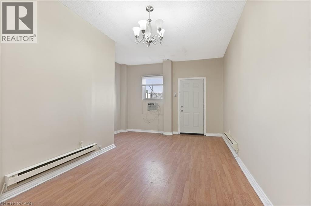Open-concept room featuring wood-finish flooring, neutral wall tones, and a multi-arm chandelier - 238-242 King Street E, Hamilton, ON