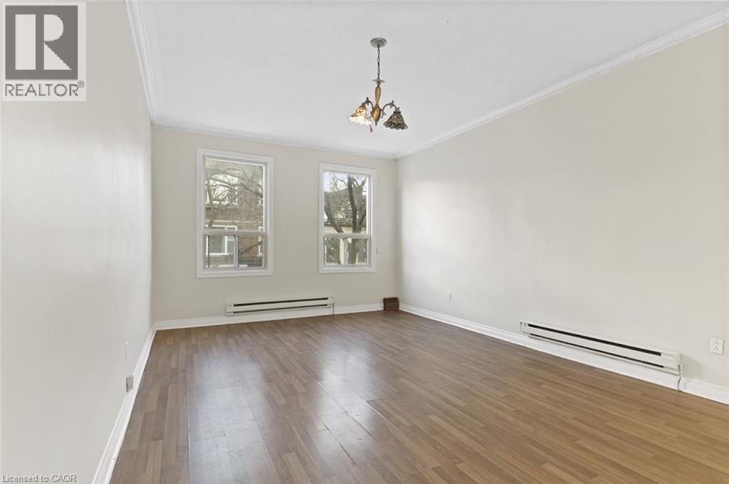 Spacious room featuring wood-finish flooring, two large windows, crown molding, and a decorative ceiling fixture - 238-242 King Street E, Hamilton, ON