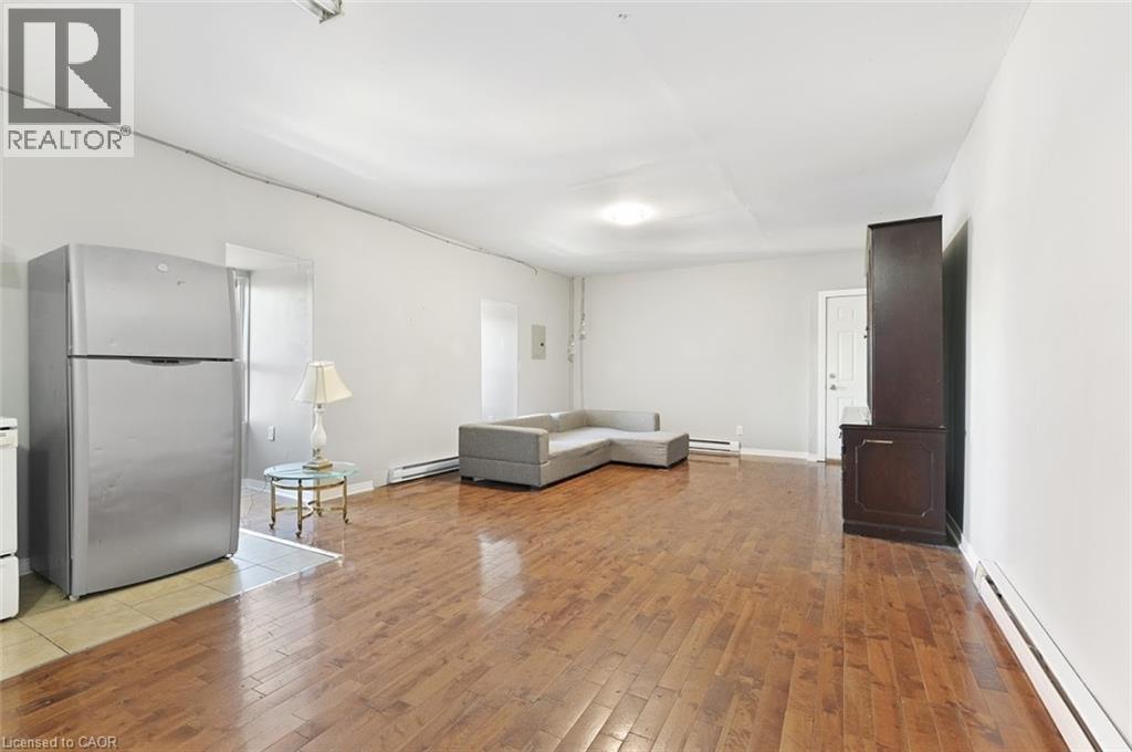 Open-concept living area featuring rich wood-finish flooring throughout, light gray walls, and a white ceiling - 238-242 King Street E, Hamilton, ON