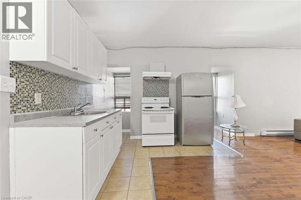 Kitchen area featuring white cabinetry with silver-tone hardware, a mosaic tile backsplash, and light-toned countertops - 238-242 King Street E, Hamilton, ON