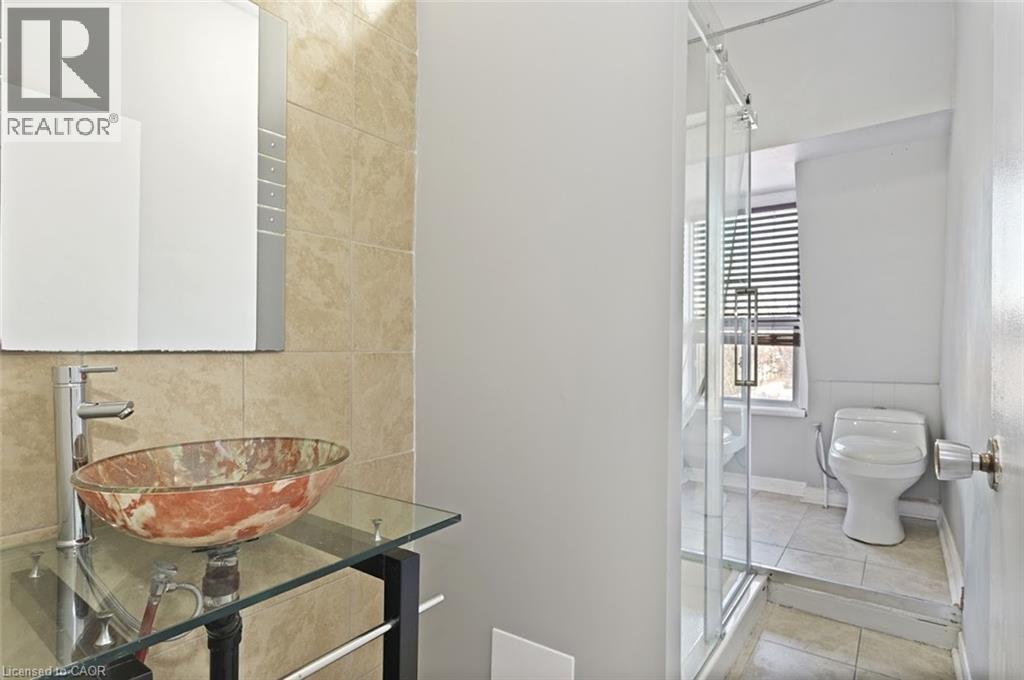 Bathroom with a vessel sink on a glass-top vanity, chrome faucet, wall-mounted mirror, and tiled walls - 238-242 King Street E, Hamilton, ON